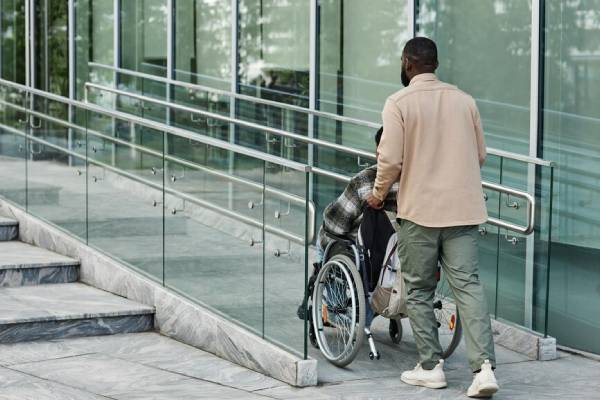 NDIS Transport Assistance: Man pushes person in wheelchair up a ramp