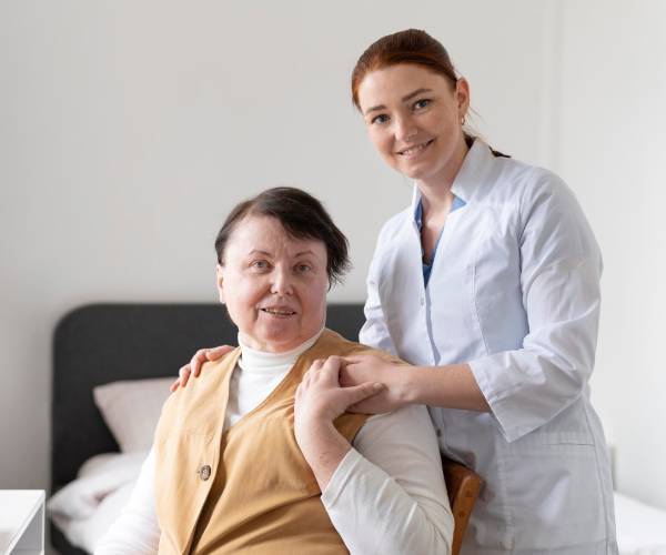 A nurse wearing a stethoscope smiles at an elderly woman on a couch