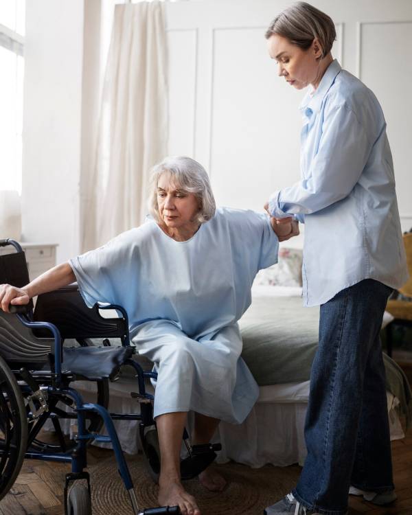 A nurse writing on a clipboard, assisting an elderly woman in a wheelchair for NDIS Nursing Care service