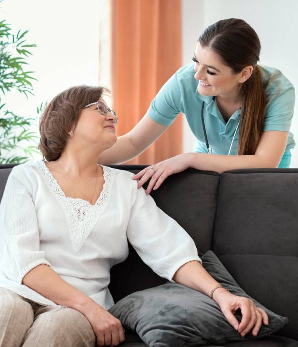 A caregiver in PPE assists an elderly woman using a walker for Complex Care Services