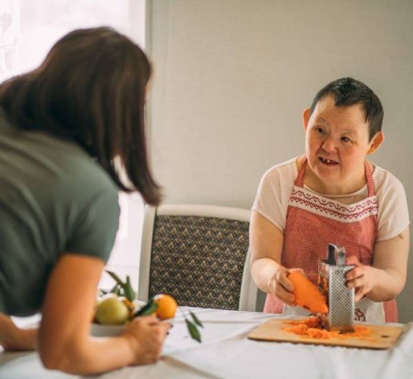 Woman with Down syndrome being taught how to grate food - NDIS Life Skill Development