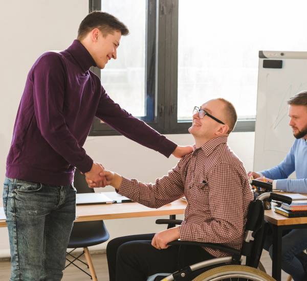 Man in wheelchair shaking hands with colleague in an office
