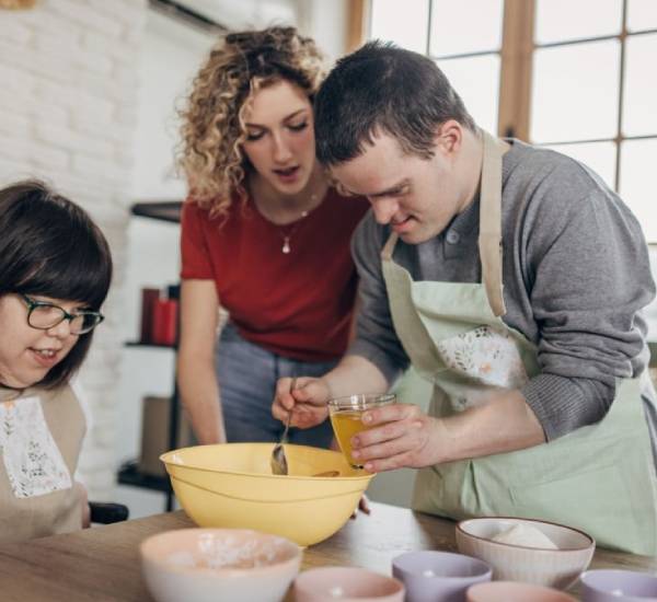 Support worker helps two young people mix ingredients - NDIS Household Task