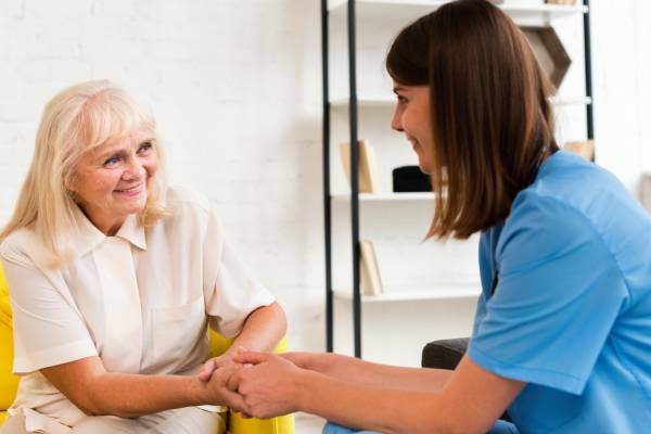 Smiling senior woman holding hands with NDIS service provider indoors