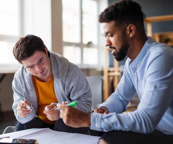 An NDIS Personal Care worker assists a young man with a learning activity