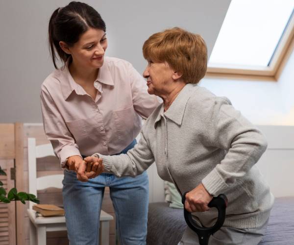 An NDIS Personal Care worker helps an elderly woman stand up
