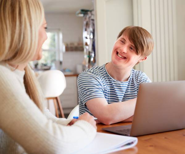 A young man with Down Syndrome smiles while learning with an NDIS SIL Providers worker