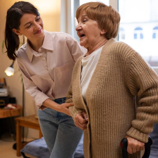 A woman in a blue shirt sits on a couch, talking to an NDIS SIL Providers worker